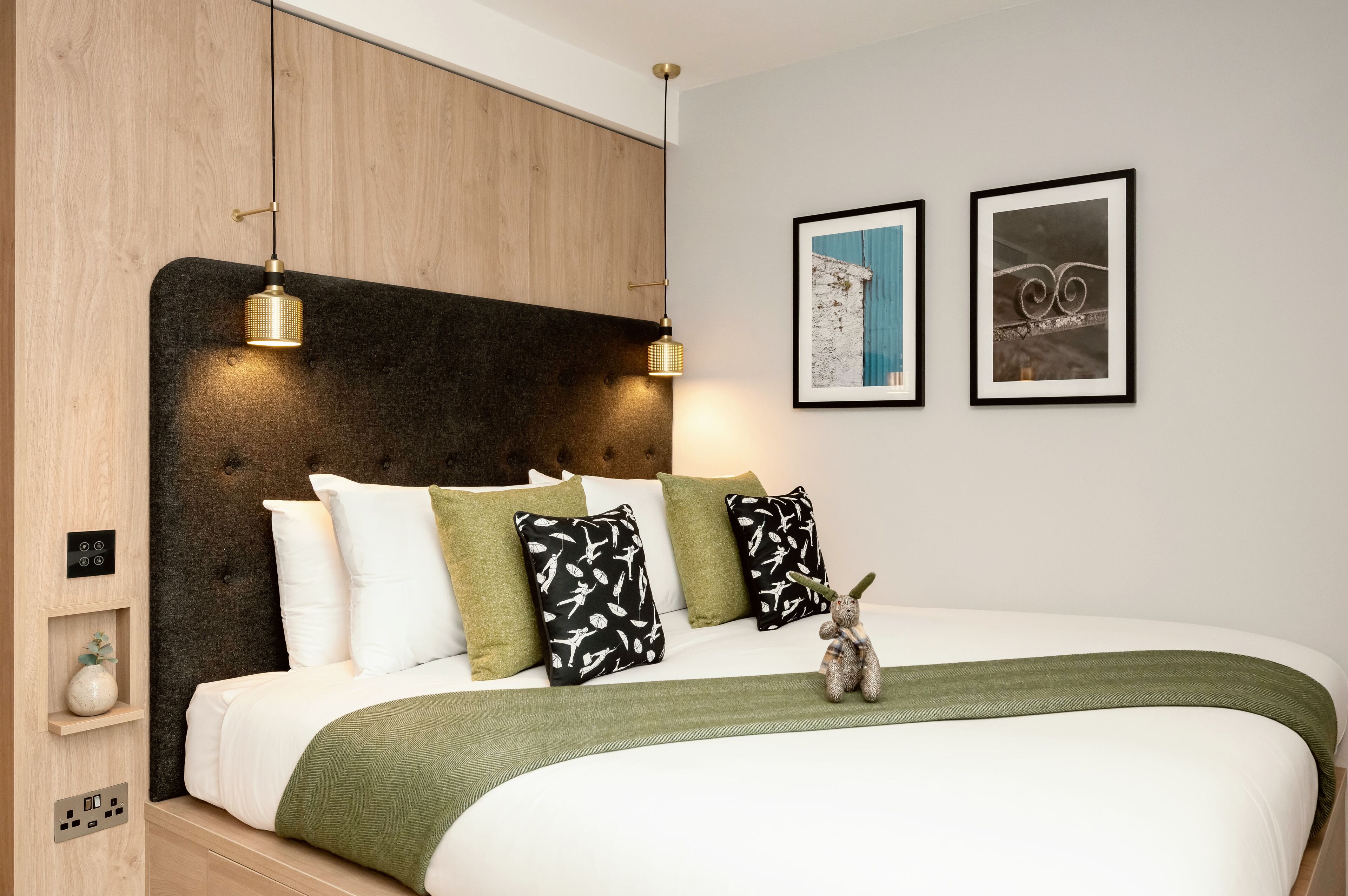 A modern bedroom with a wooden headboard, a green throw blanket, and two framed pictures on the wall.