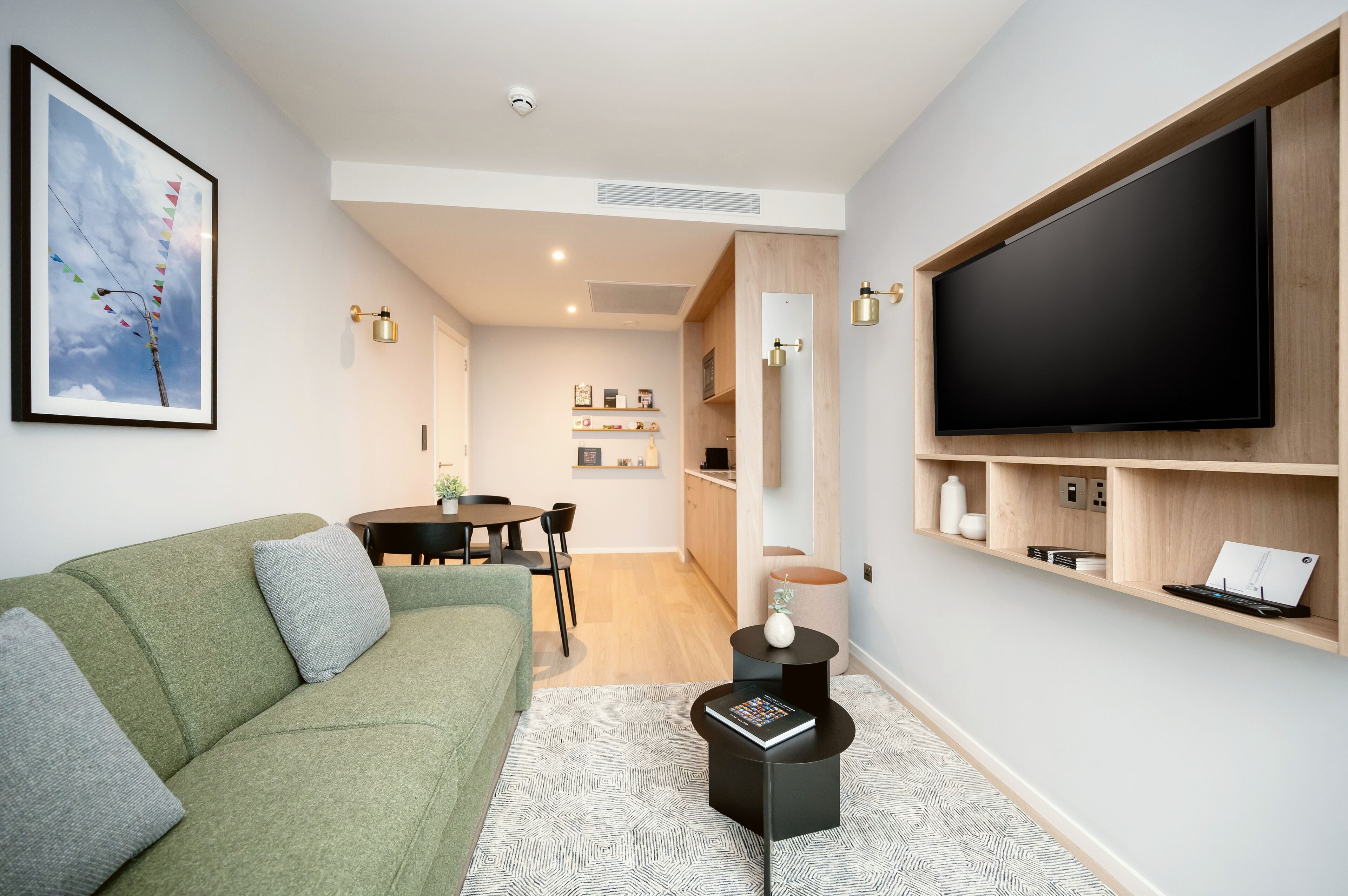 A modern living room with a green sofa, a flat-screen TV, and a dining area with a table and chairs.