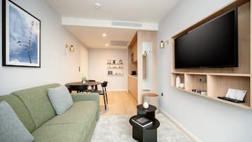 A modern living room with a green sofa, a flat-screen TV, and a dining area with a table and chairs.