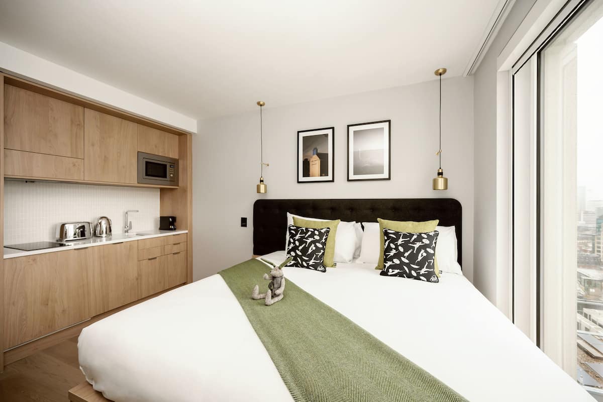 A hotel room with a bed, a kitchenette, and a city view.
