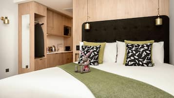 Una cama impecable con un cubrecolcha verde, cabecera con dos lámparas colgantes y una pequeña figura decorativa de conejo.