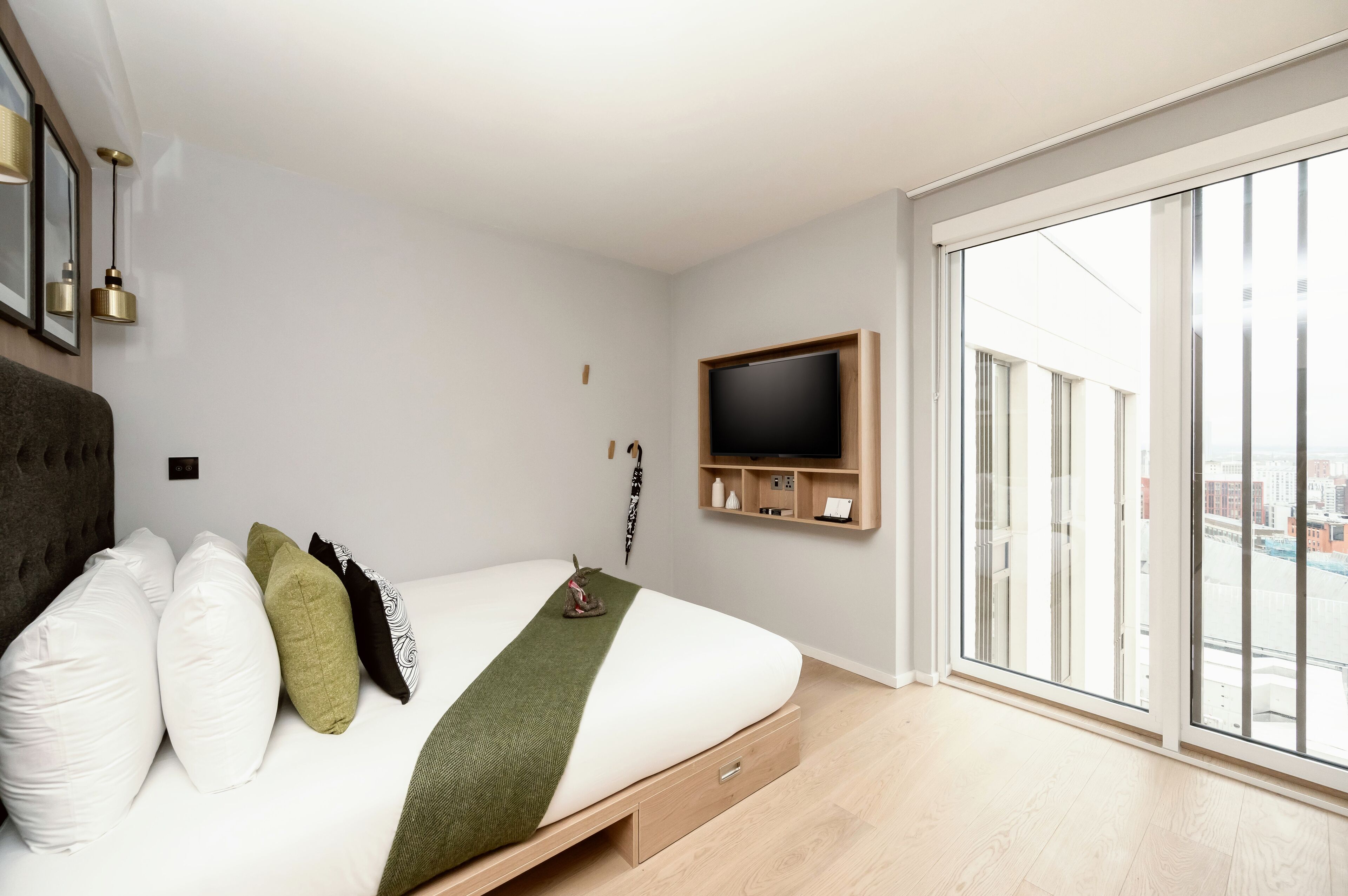 A modern bedroom with a bed, pillows, a TV, and a large window.