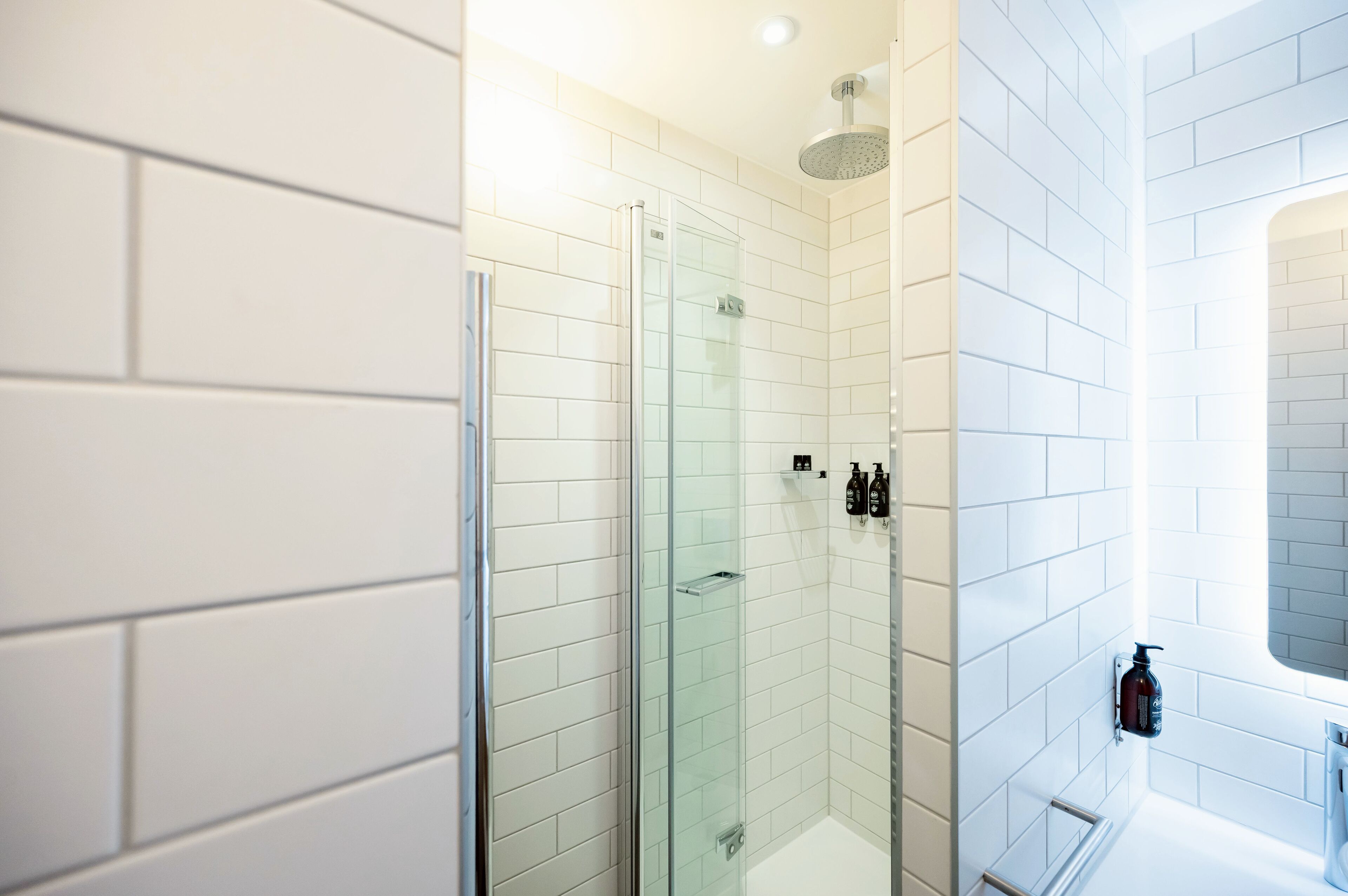 A modern bathroom with white subway tiles, a glass shower enclosure, and a built-in sink with a mirror.