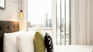 Una habitación de hotel moderna con vistas a la ciudad, cabecera tapizada y una lámpara colgante.