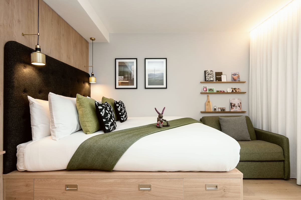 A modern bedroom with a large bed, a green sofa, and a wooden headboard.