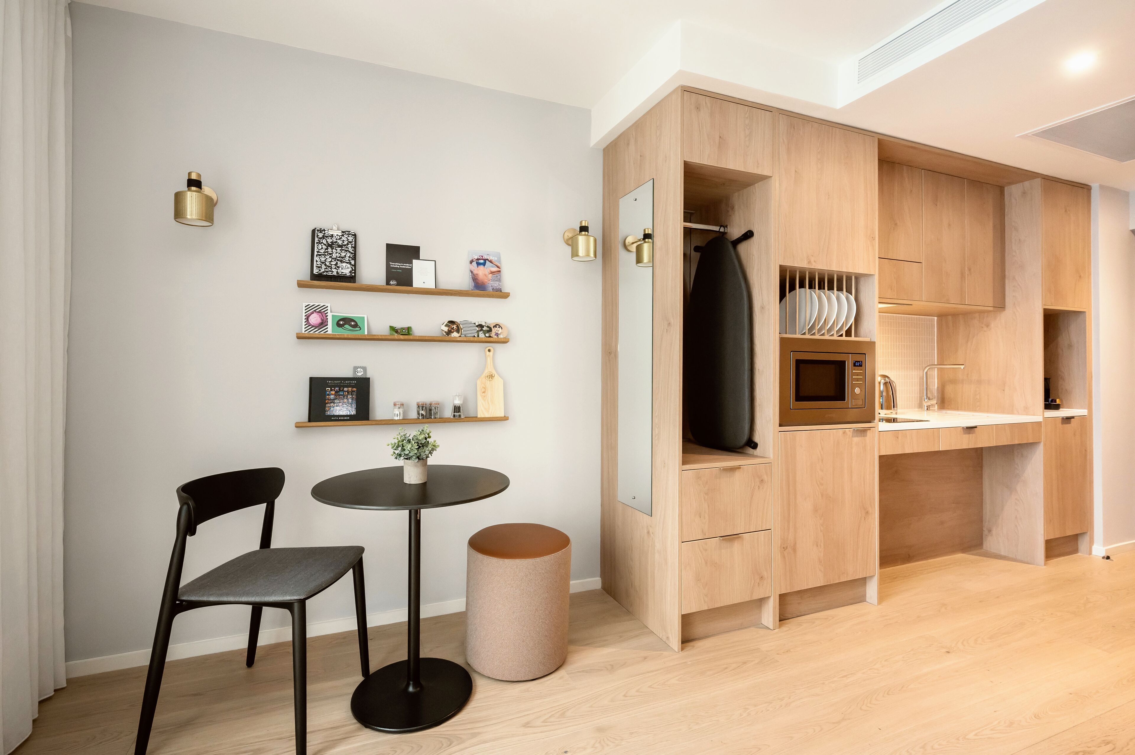 Cocina compacta con armarios de madera, un microondas y un pequeño comedor con una silla y una mesa.