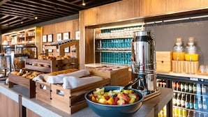 Un bufé de desayuno con diversas opciones de pastelería, un bol de fruta y una máquina de café.