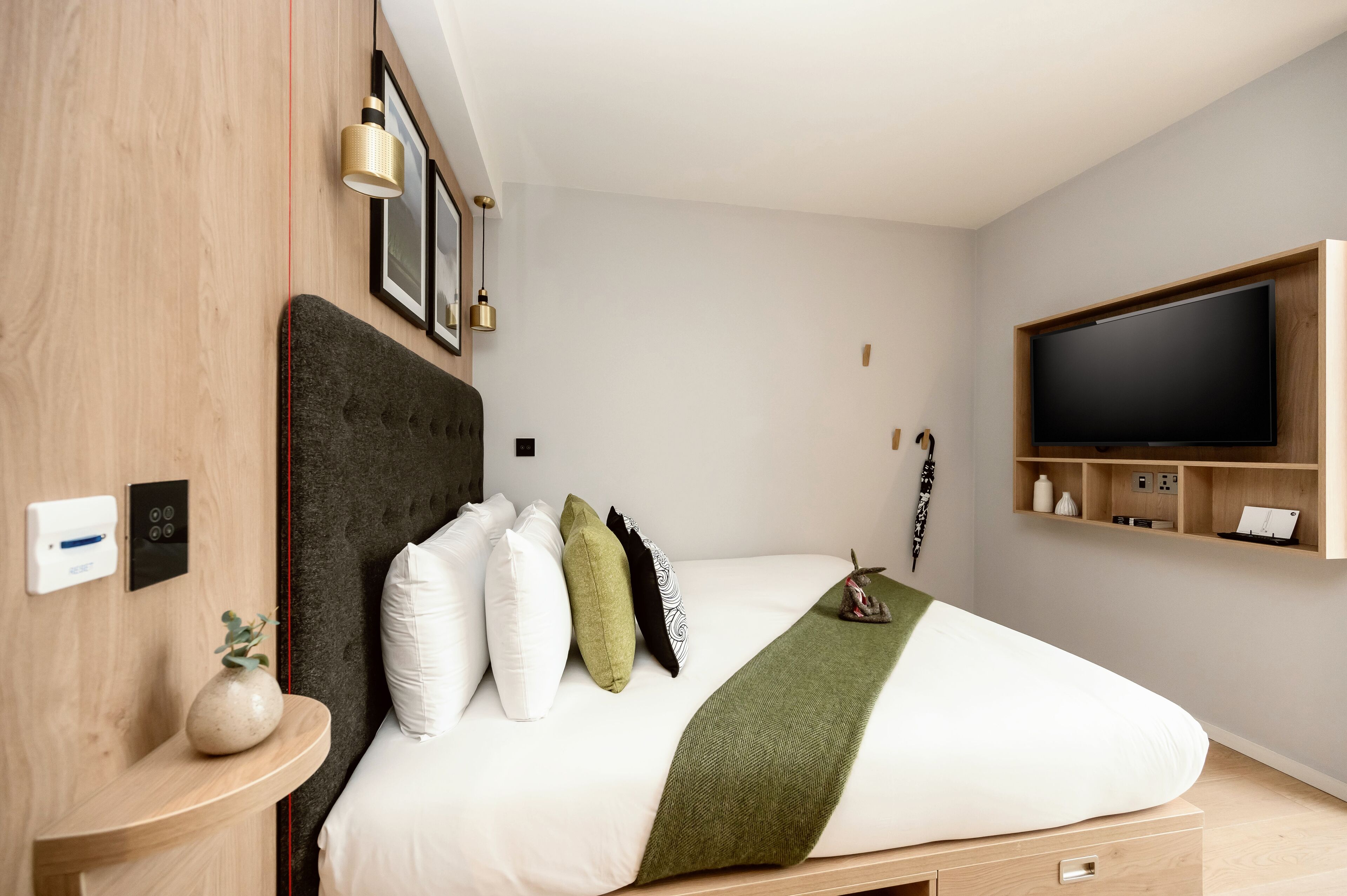 A modern bedroom with a large bed, a TV mounted on the wall, and a bedside table with a vase.