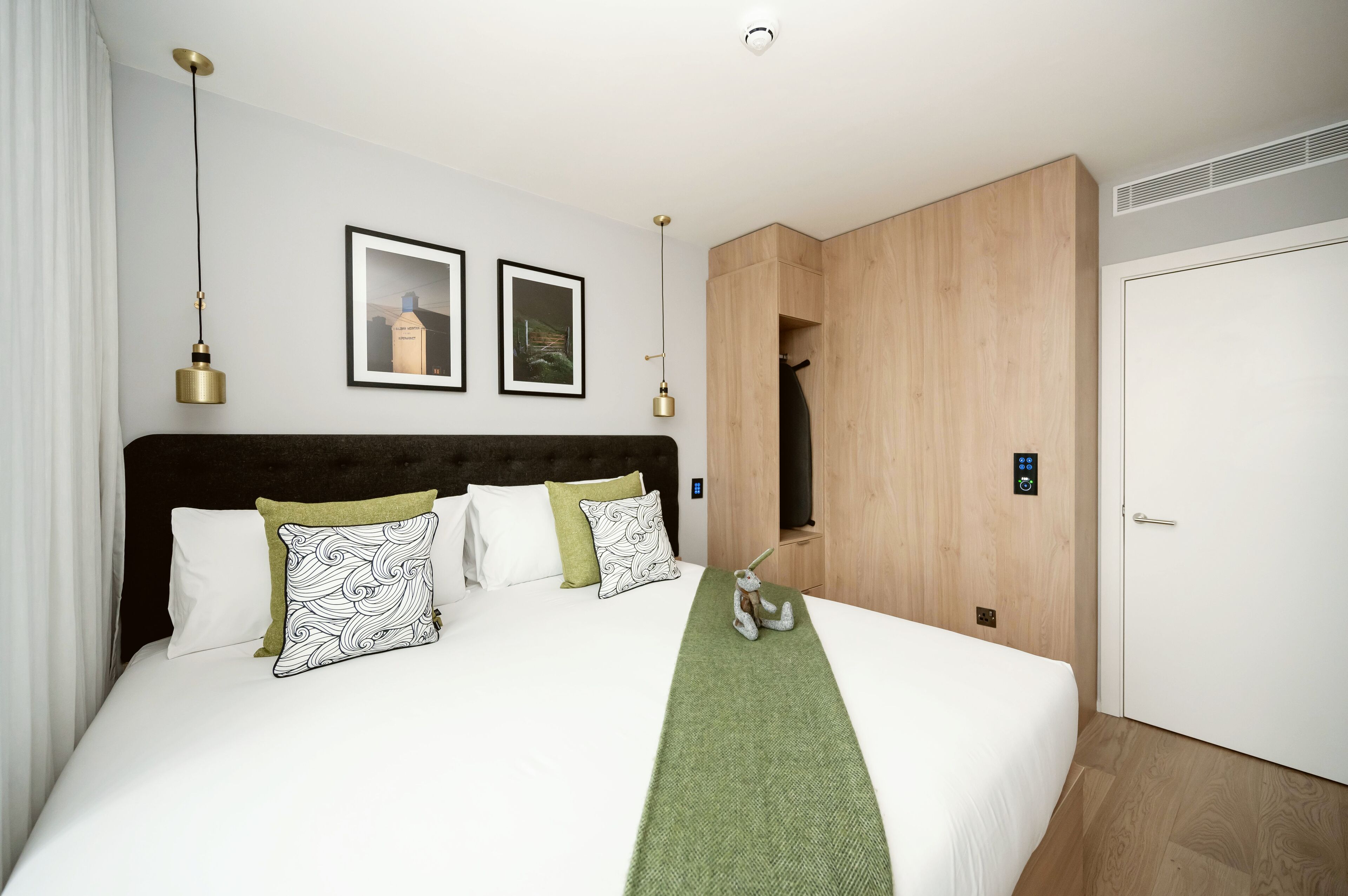 A modern hotel room with a large bed, a wooden wardrobe, and a framed picture on the wall.