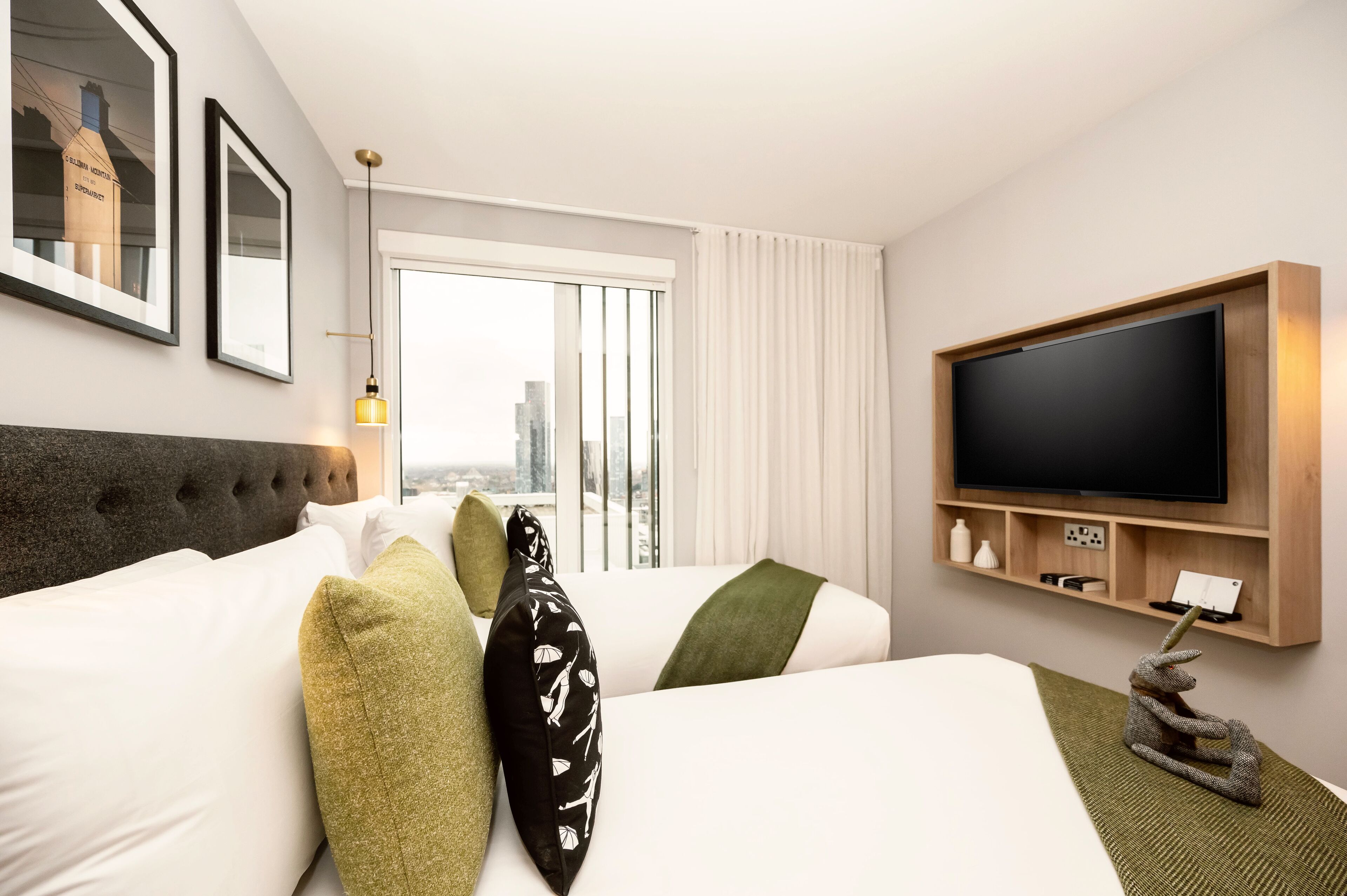 Une chambre d’hôtel avec un grand lit, un téléviseur à écran plat fixé au mur, une fenêtre avec des rideaux et des tableaux encadrés accrochés au mur.
