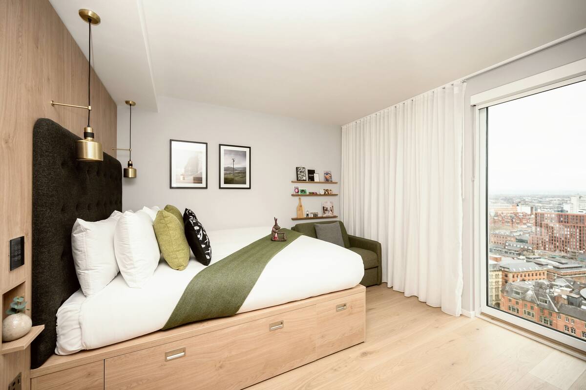 A modern bedroom with a large bed, a view of the city, and a cityscape visible through the window.