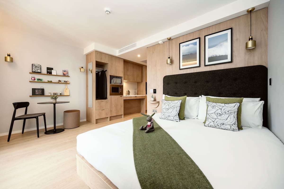 A modern hotel room with a large bed, a desk, and a kitchenette.