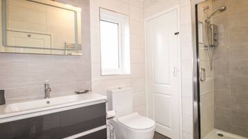 Une salle de bain moderne avec un lavabo blanc, un meuble-lavabo, des toilettes et une douche à parois de verre.