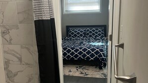 Um banheiro com chuveiro, tapete escuro e cama com colcha estampada.