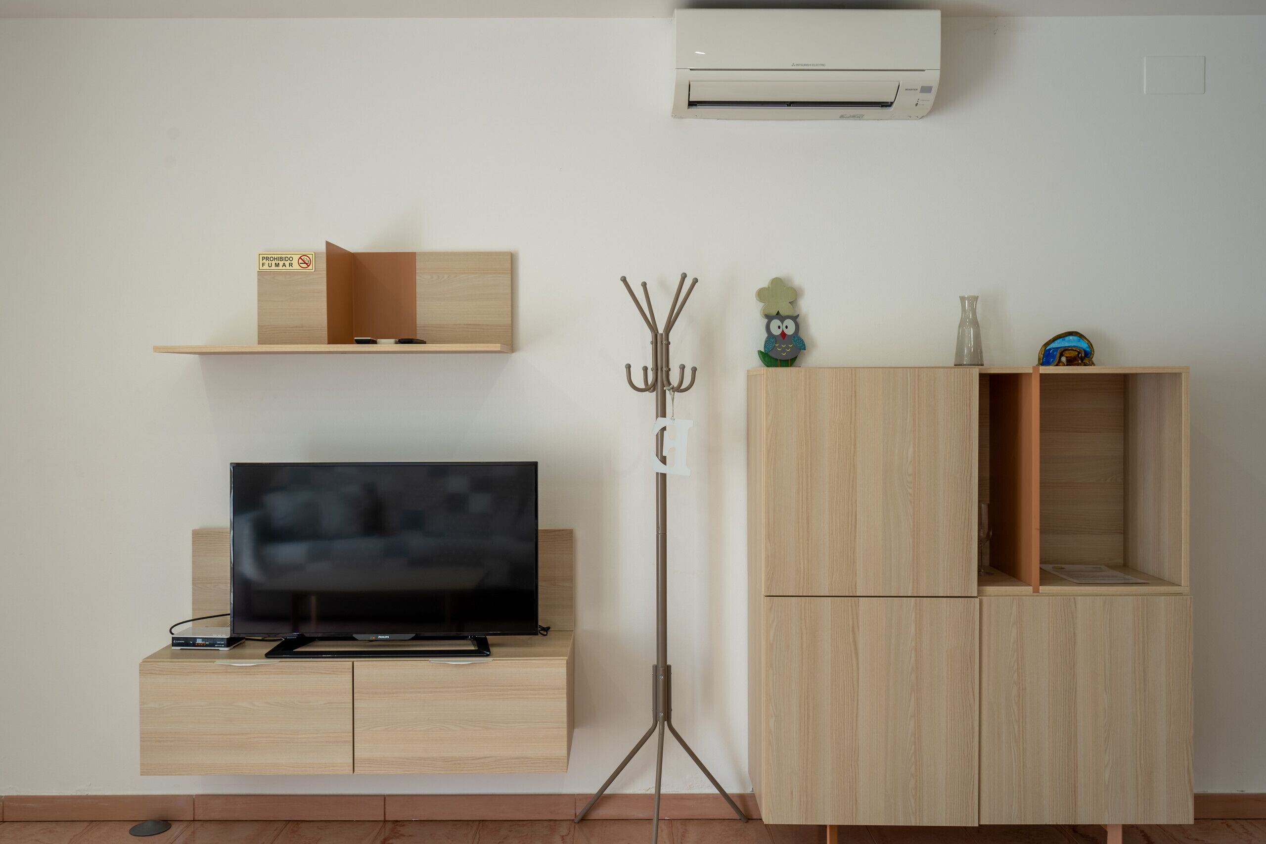 A modern living room with a flat-screen TV, a wooden cabinet, a wall-mounted air conditioner, and a decorative owl ornament.