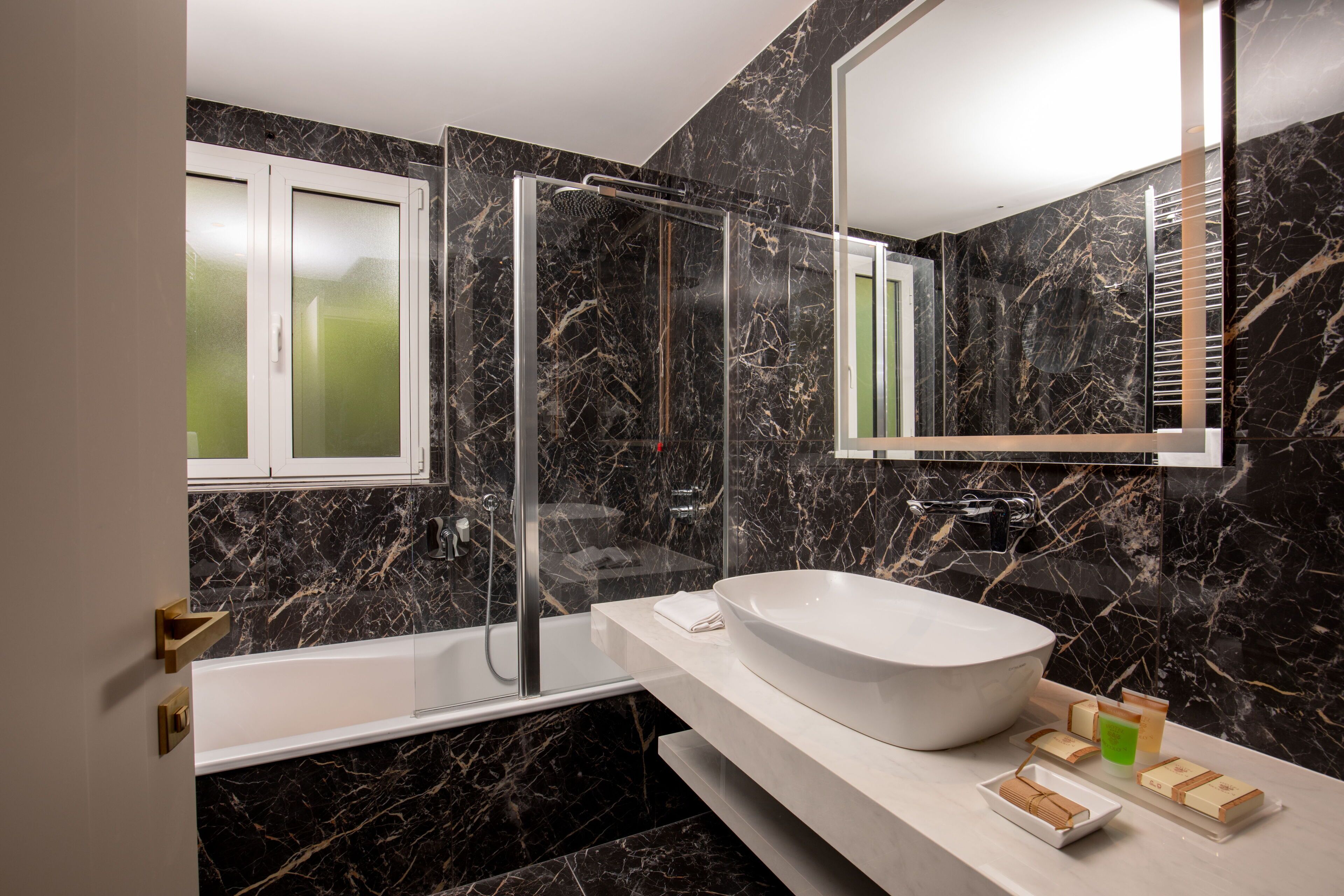A modern bathroom with a large white sink, a glass-enclosed shower, and marble walls.