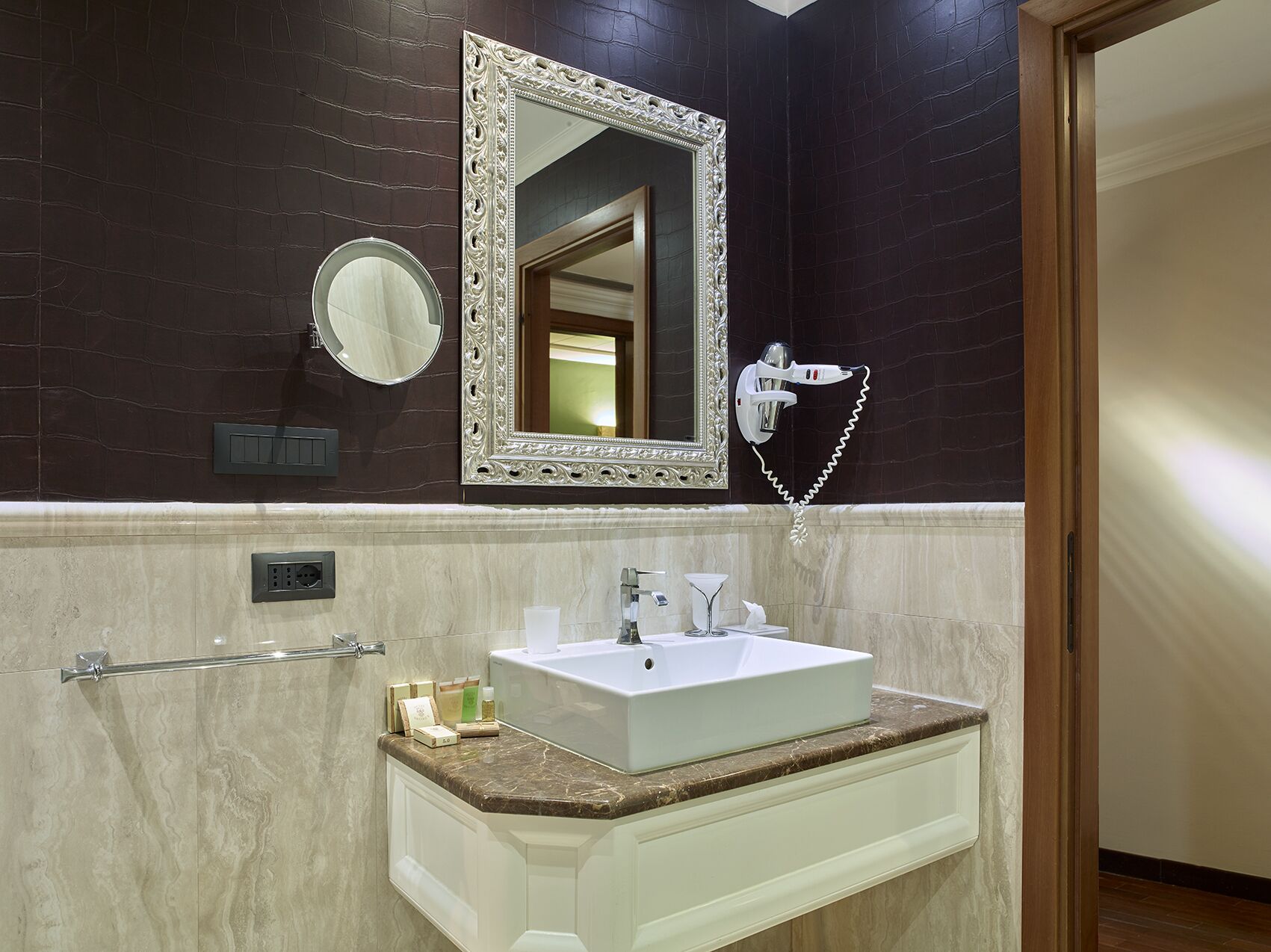 A bathroom with a large mirror, a hairdryer, a sink, and toiletries on the countertop.