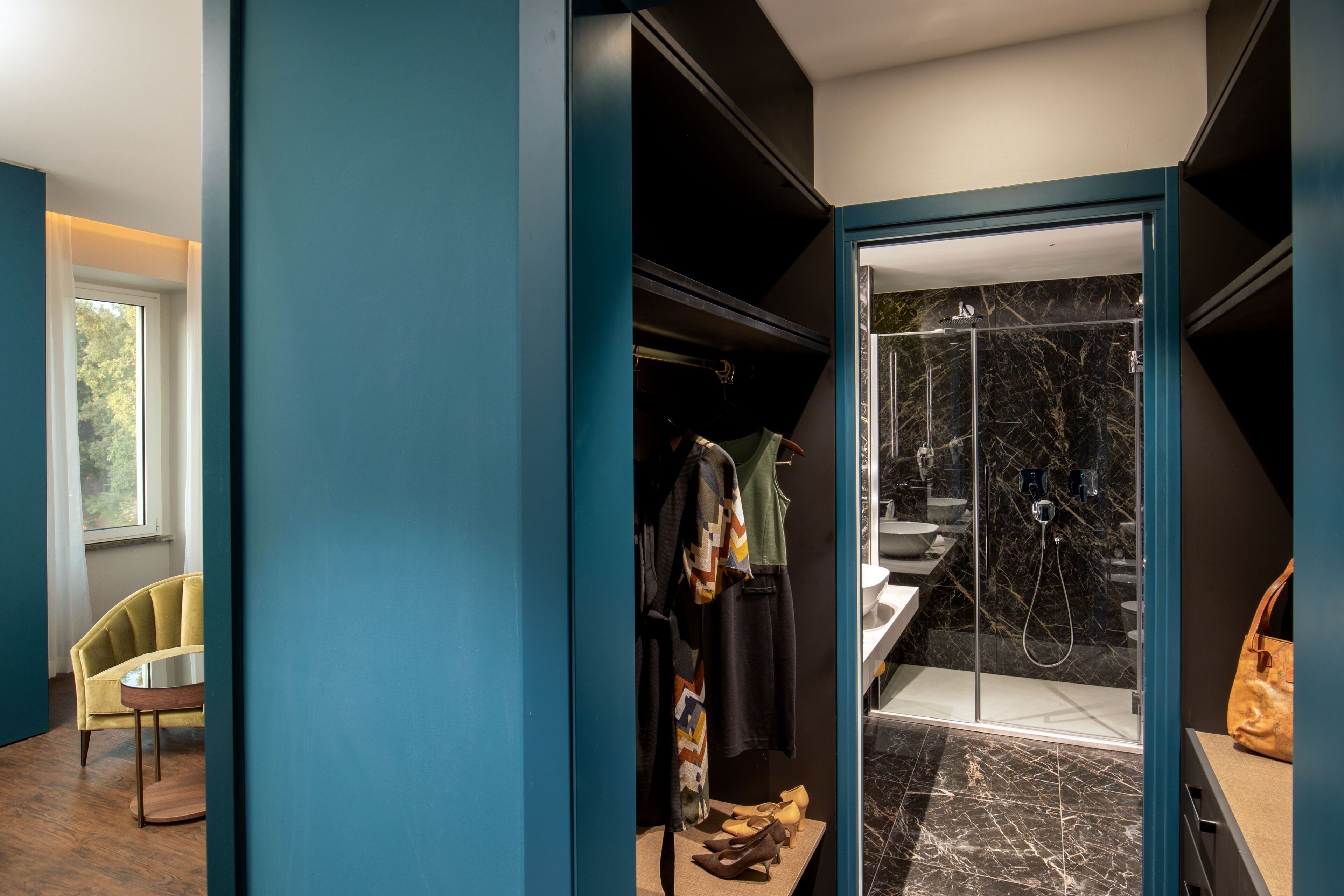 Un baño moderno con cabina de ducha de vidrio, tocador con encimera de mármol y perchero con varias prendas.