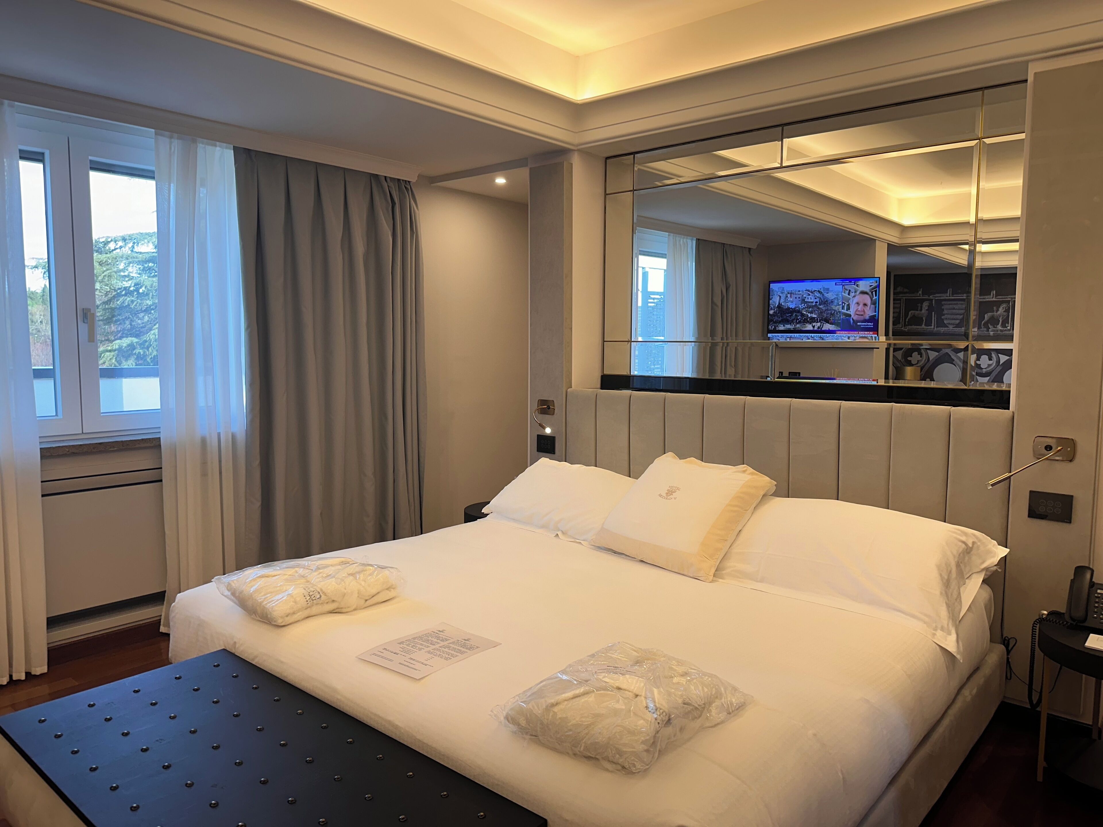 Una habitación de hotel con una cama grande, una mesita de noche, un espejo y un televisor en la pared.