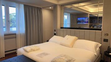 Une chambre d’hôtel avec un grand lit, une table de chevet, un miroir et un téléviseur fixé au mur.