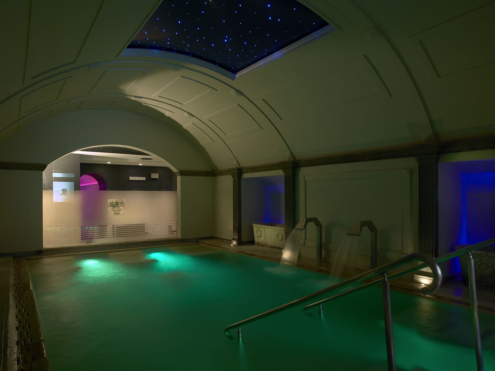 A spacious indoor swimming pool with a starry sky ceiling and a view of the cityscape.