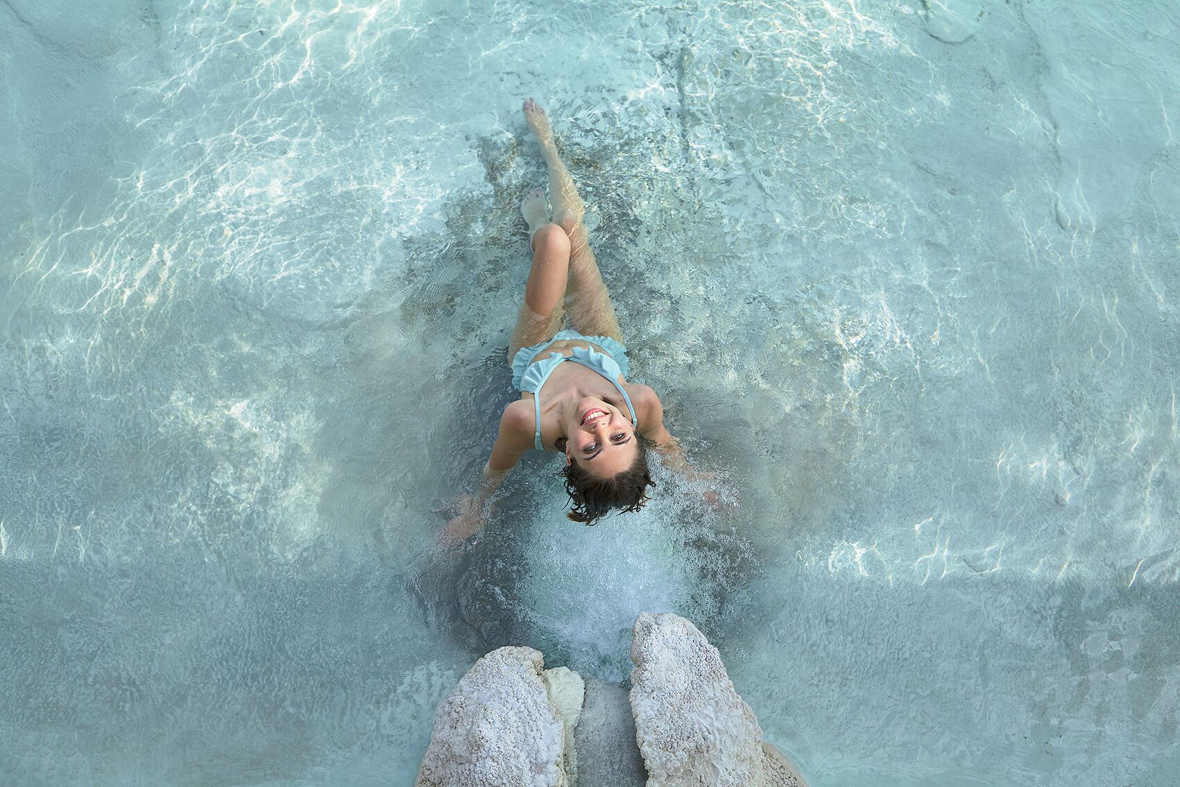 A person floating in a clear pool with a rock at the bottom.