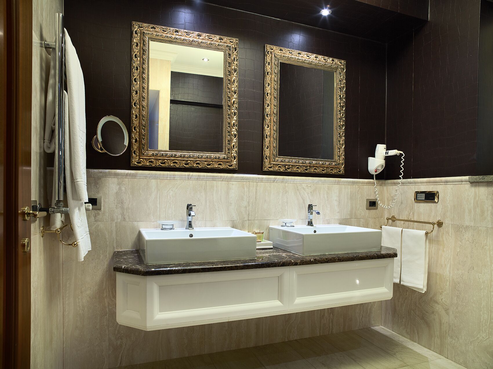 A bathroom with two sinks, a vanity, a towel rack, and two large mirrors with ornate frames.