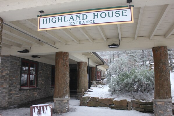 A covered entrance to Highland House with stone pillars and a snow-covered landscape. - Highland House, Central Village, Overlooks slopes, sky stage, balcony (Snowshoe)