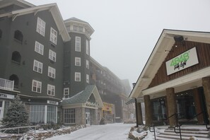 A hotel with a snow-covered entrance, a sign for 'ABAS' restaurant, and a 'Highland Lodge' building in the background. - Highland House, Central Village, Overlooks slopes, sky stage, balcony (Snowshoe)