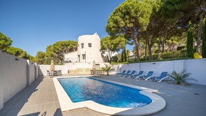 Une piscine avec des chaises longues et un bâtiment blanc en arrière-plan.