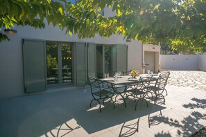 An outdoor patio with a table set for dining, surrounded by chairs, and a glass door leading to an interior space.