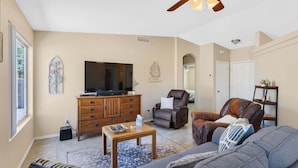 A living room with a ceiling fan, a television, a leather chair, a sofa, and a wooden cabinet. - Peaceful Valley - Rita Ranch/Tucson- 3BR/2BA/PrivatePool/NearShops&Restaurants (Tucson)