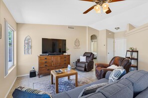 A living room with a ceiling fan, a television, a leather chair, a sofa, and a wooden cabinet.