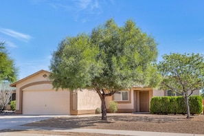 A residential house with a garage, a well-maintained lawn, and a small tree in the front yard.