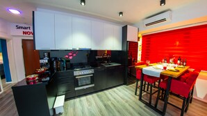 Une cuisine moderne avec des appareils électroménagers noirs, un coin repas avec des chaises rouges et un mur d’accent rouge.