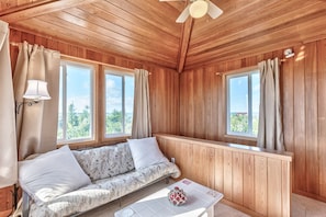Una stanza accogliente con pareti in legno, un divano, un tavolo e ampie finestre che si affacciano sul verde.