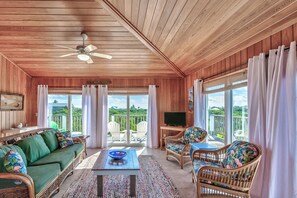 A wooden-paneled room with a green sofa, wicker chairs, a table with a bowl, and a TV. - Lookout House - Discover Tranquility (Hope Town)