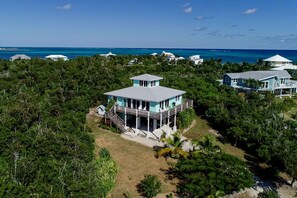 A coastal house with a large deck, surrounded by dense tropical vegetation and a clear view of the ocean. - Lookout House - Discover Tranquility (Hope Town)