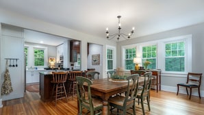 Una cocina amplia con suelo de madera, una zona de comedor con mesa y sillas de madera, y ventanas grandes con vistas al verdor.
