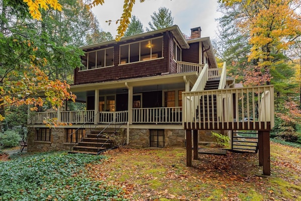 A two-story house with a stone foundation, a balcony, and a wooden deck. - Birdwood | Renovated Historic Montreat Home with Deck, Fire Pit & 2 Grills! (Montreat)