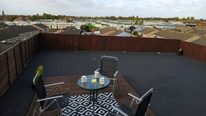 A rooftop terrace with a table and chairs, a view of a residential area, and a wooden fence. - Roman Bank Flat With Spa Bath and Mermaids Teepee (Skegness)