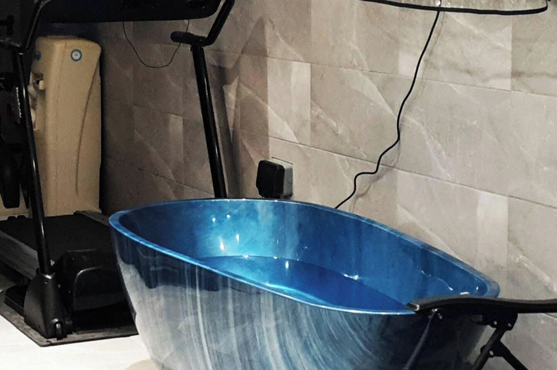 A blue bathtub in a bathroom with a tiled wall and a black chair.