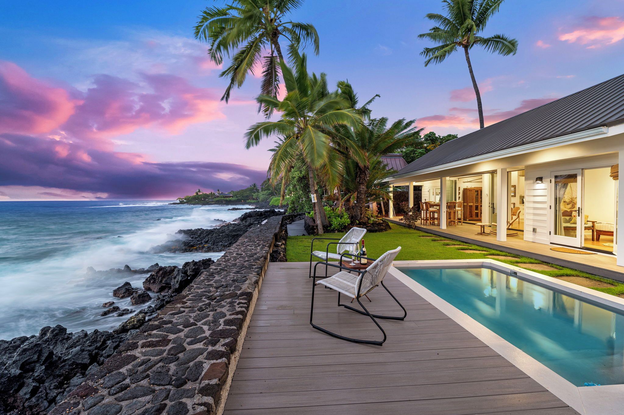 A poolside area with a view of the ocean, a wooden deck, and a building with glass doors.