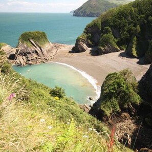 A coastal landscape with a beach, cliffs, and a clear view of the sea.