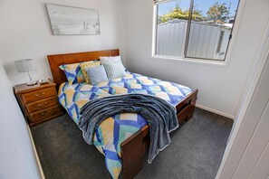 A bedroom with a wooden bed, a nightstand, a lamp, and a window with a view of a fence.
