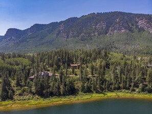 Una cabaña junto al lago, rodeada de un bosque denso y montañas.