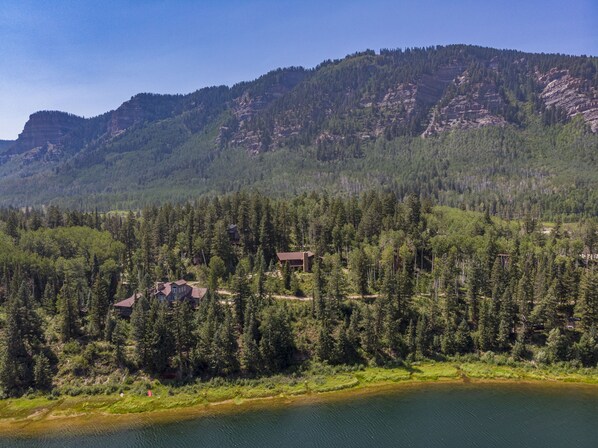 A lakeside cabin surrounded by dense forest and mountains.