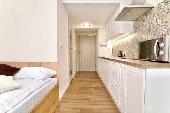 Un estrecho pasillo que conduce a un dormitorio y una kitchenette con armarios blancos y un microondas.