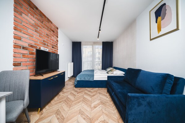 A modern living room with a brick wall, a flat-screen TV, a blue sofa, and a herringbone-patterned floor. - ICE Apartments (Kraków)