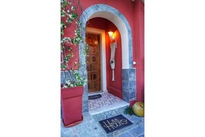 A red-walled entrance with a wooden door, a hanging plant, and a 'Hello' mat.
